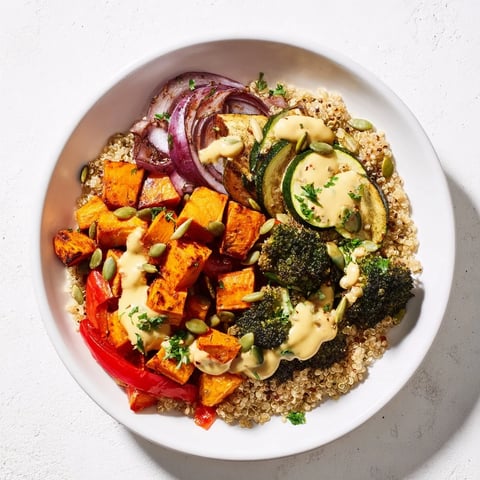 Vibrant Quinoa Bowl with roasted seasonal veggies, drizzled with creamy lemon-tahini dressing and optional toppings.