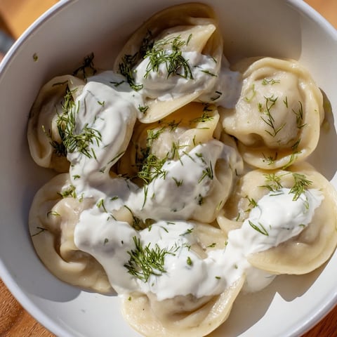 Steaming hot Russian pelmeni, savory meat dumplings swimming in creamy sour cream, ready to enjoy.