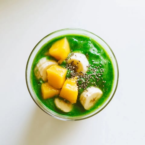 A tall glass of Spinach-Hidden Smoothie with vibrant green hues, garnished with a fresh mango slice and chia seeds, enjoyed as a refreshing morning boost.