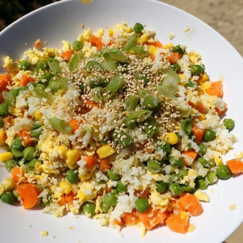 A bowl of colorful, savory Frozen Veggie Fried Rice, garnished with fresh green onions and sesame seeds.