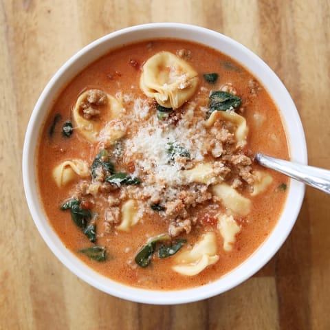 Freshly ladled Tuscan Tortellini Soup steaming in a wide pot, featuring tender tortellini, savory sausage crumbles, and vibrant spinach leaves.