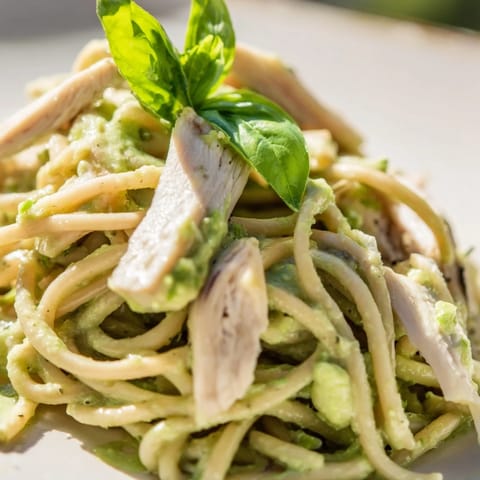 A close-up shows creamy avocado chicken pasta tossed with basil, ready to be served with lemon zest and Parmesan.