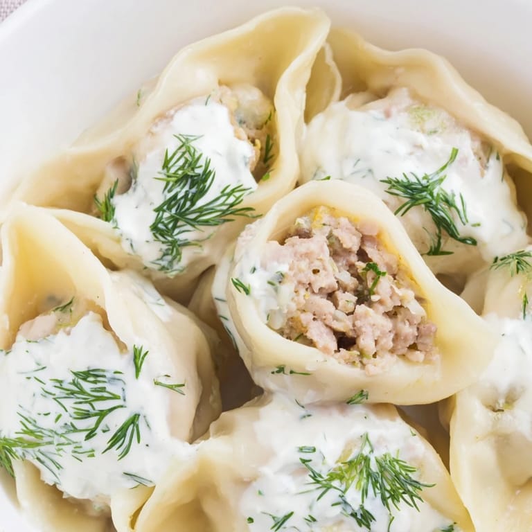 A heaping plate of homemade Russian pelmeni, their savory meat filling visible beneath the creamy topping.